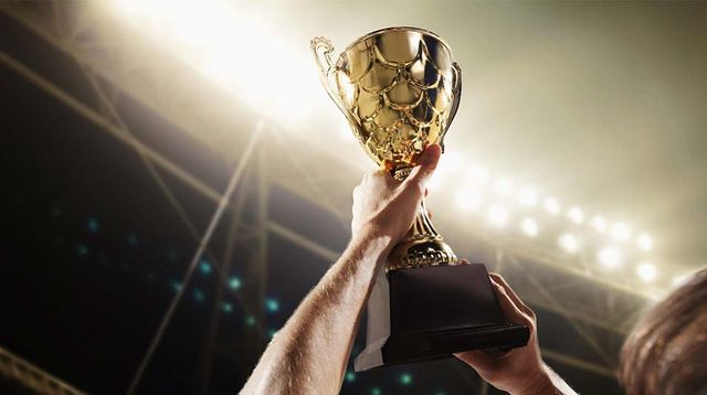 Jubelnder Sportler hält goldene Sieger-Trophäe hoch auf der Bühne.